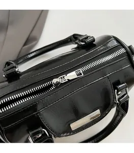Detailed view of glossy black cylinder bag showing smooth silver zipper and leather texture