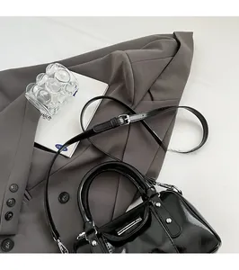 Top view of black patent leather cylinder bag on grey blazer with a metal zipper