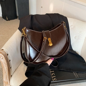 Glossy dark brown retro shoulder bag with gold clasp shown on a white French armchair