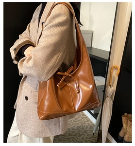 Side view of large brown faux leather tote bag with ribbon knot on a female model