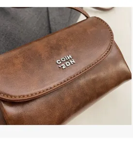 Gros plan du sac en cuir PU marron vintage avec texture mate et lettrage en métal argenté