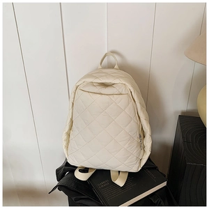 Détail d'un sac à dos matelassé beige montrant le motif de losanges et zip métallique