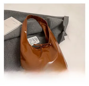 Close-up of brown glossy hobo bag with bow detail on grey coat and white bedding