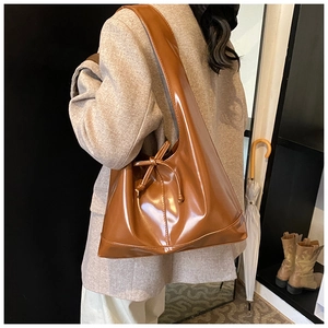 Detail of caramel brown glossy shoulder bag with bow and minimalist triangular shape