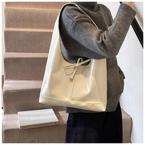 Close-up of a cream patent leather tote bag with decorative drawstring bow detailing