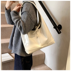 Close-up of cream glossy tote bag featuring a decorative bow and wide shoulder strap