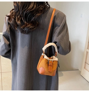Brown suede bucket bag with white plush trim and metal buckle on grey blazer