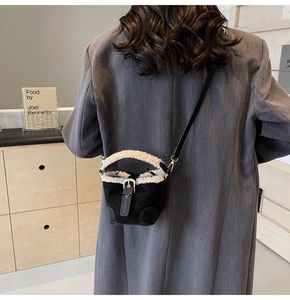 Detail of mini black and white plush bucket bag worn crossbody in a minimalist setting