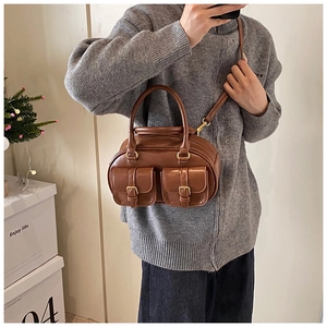 Brown vintage bowling handbag with gold buckle pockets worn as a stylish crossbody bag