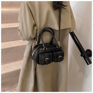 Chic black bowling handbag with gold buckle pockets styled on model in brown coat