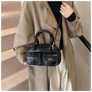 Detail view of a black glossy bowling bag with gold buckle pockets on a trench coat