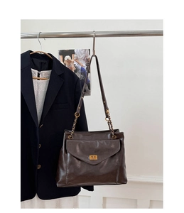 Detail of deep brown shoulder bag featuring gold twist lock and chain strap on display