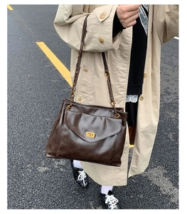 Detail of dark brown leather tote featuring gold metal lock and chain strap on shoulder