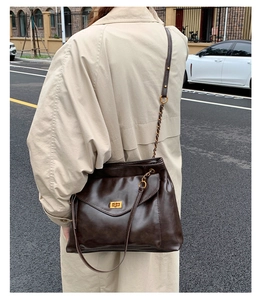 Outdoor street view of a stylish dark brown leather chain tote bag on a beige trench coat