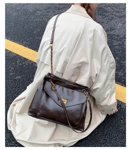 Detail of coffee brown tote with golden twist lock and chain strap on a trench coat