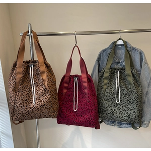 Three leopard print drawstring tote bags in brown, red, and green on metal hangers