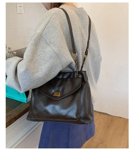 Detail of black leather shoulder bag with gold twist lock and chain strap on a model