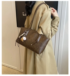 Detail of dark brown leather tote bag with creative baseball charm and long shoulder straps