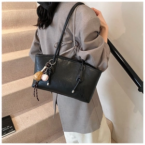Detail of black faux leather tote bag featuring unique knot straps and baseball charms