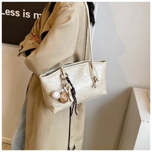 Detail of beige tote bag with litchi grain texture and baseball glove charm