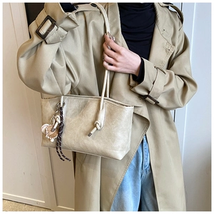 Close-up of cream tote bag with leather texture, knotted straps and baseball charms