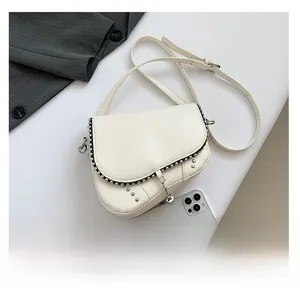 Vue détaillée du sac besace blanc avec clous et chaîne sur une veste de blazer grise