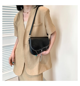 Détails d'un sac besace vintage en cuir noir avec des rivets et des glands en chaîne