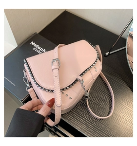 Détail d'un sac besace rose avec rivets argentés et chaîne métallique sur une surface boisée