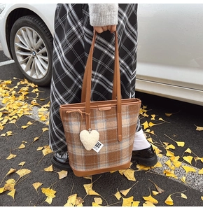 Détail d'un cabas en laine à carreaux avec charm en peluche en cœur et poignée en cuir brun