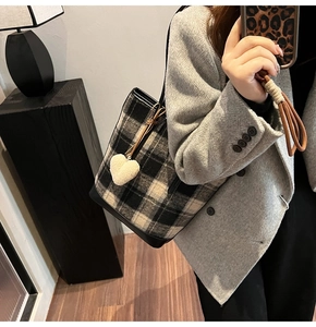 Détail du sac seau à carreaux avec breloque cœur porté sur un blazer gris chic