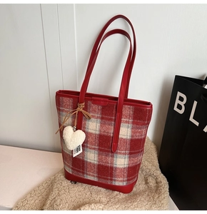 Detail of red checkered tote bag featuring a white plush heart charm and leather trim