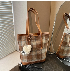 Détail du sac cabas à carreaux avec un charm coeur en peluche et bordure en cuir marron