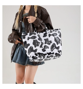Model showing a large cow print tote bag with white lettering against a brown leather jacket