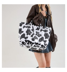 Detail shot of glossy cow print tote bag with black and white spots and text
