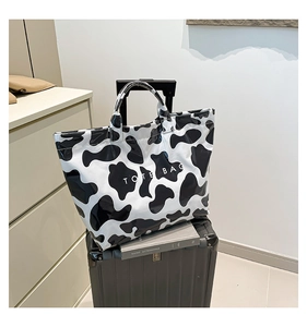 Detail of cow print tote bag with white TOTE BAG text on a suitcase for travel