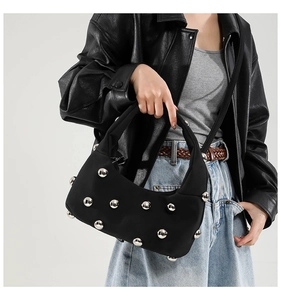 Detail of black underarm bag with silver metallic studs worn by a model in modern style