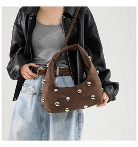 Detail of brown suede handbag with large silver metal rivets and integrated handle