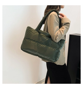 Close-up of dark green quilted puffer tote bag worn over the shoulder by a model
