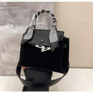 Close-up of matte black leather handbag featuring a silk scarf-wrapped handle and metal lock
