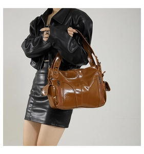 Detail of glossy brown PU leather shoulder bag featuring functional metal zippers and side pockets
