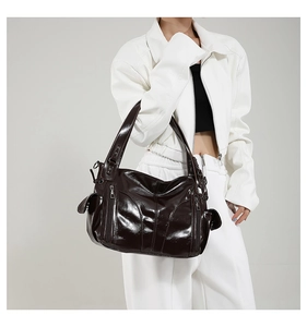 Detail of dark brown glossy PU shoulder bag with silver zippers on a white outfit