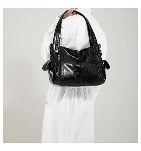 Close-up of black patent leather shoulder bag with multiple zippers and buckle details