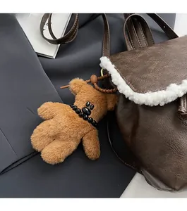 Detail of cute brown teddy bear plush keychain with black beads on a leather shoulder bag