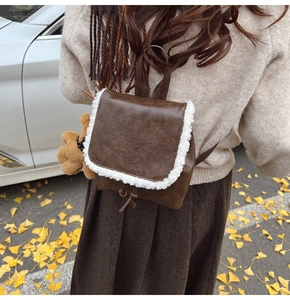 Brown leather backpack with plush trim and bear pendant shown in an autumn street scene