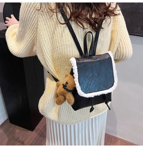 Detail of black mini backpack with faux shearling trim and cute brown plush bear pendant