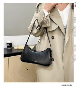 Detail of a minimalist black crescent shoulder bag on a model wearing a beige trench coat