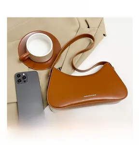 Close-up of brown crescent underarm bag with white logo and adjustable shoulder strap