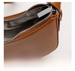 Detail view of brown leather bag showing silver zipper closure and herringbone fabric lining