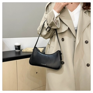 Detail of a black leather shoulder bag with a silver logo on a khaki trench coat