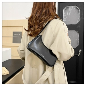 Close-up of minimalist black leather hobo bag with white lettering worn by a model